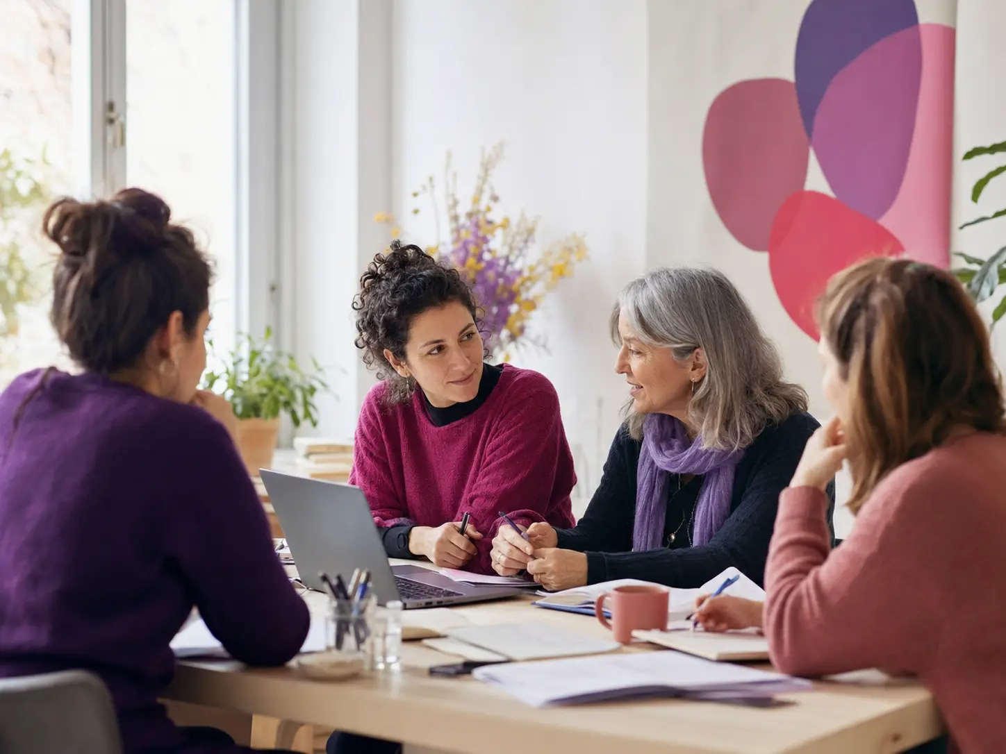 Quattro donne collaborano intorno a un tavolo durante una riunione di progettazione sociale.